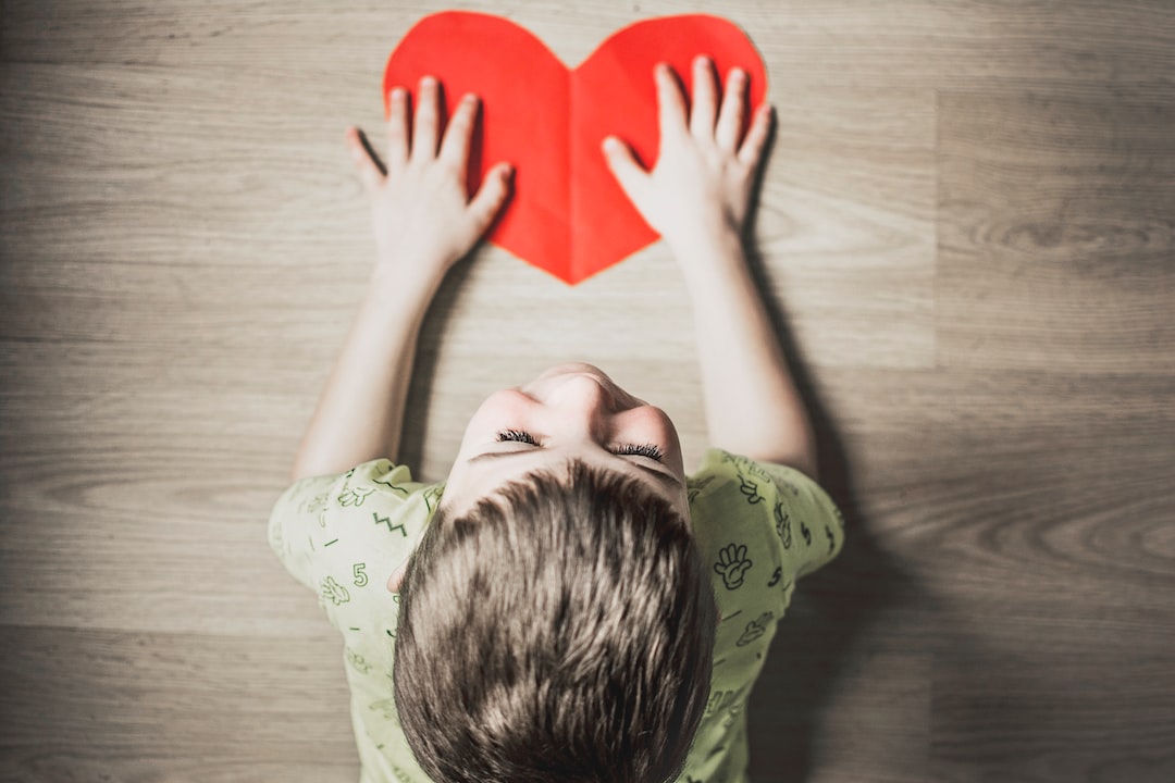 boy in green shirt holding red paper heart cutout on brown table 4R6pg0Iq5IU jpg