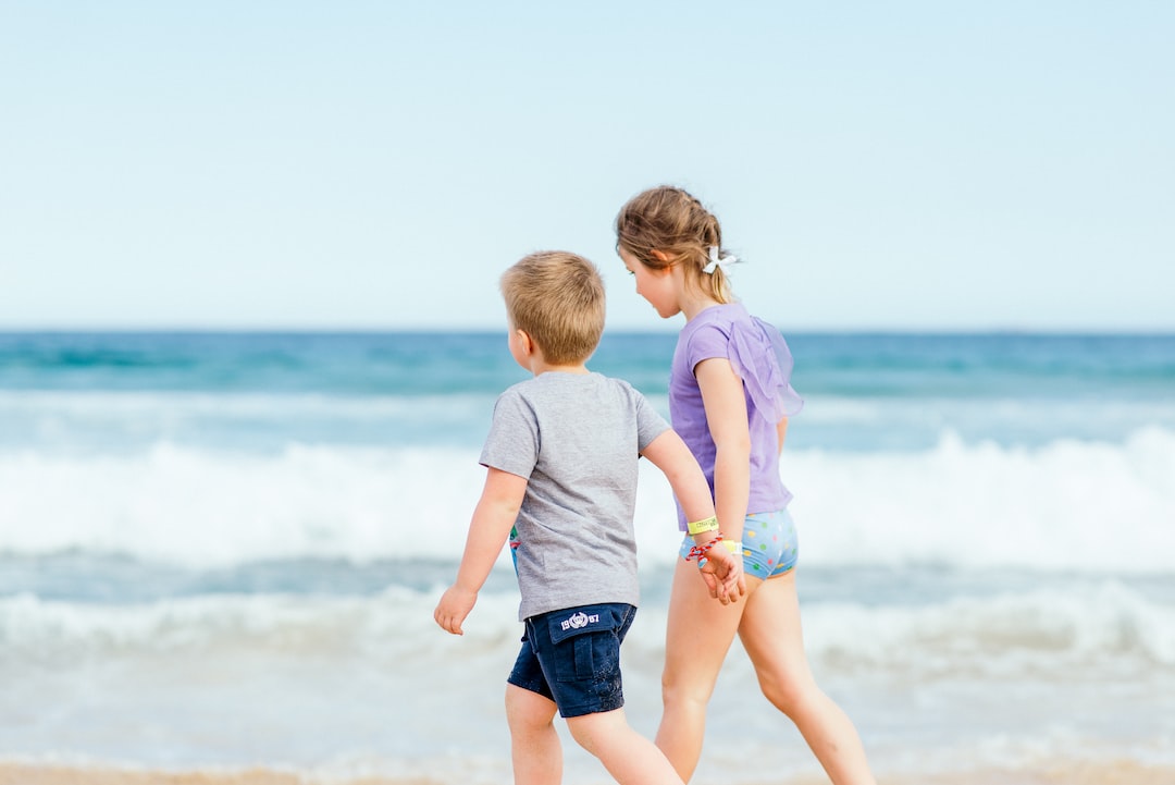 boy in white t shirt and blue shorts standing on seashore during daytime CUg2tKMHV4 jpg