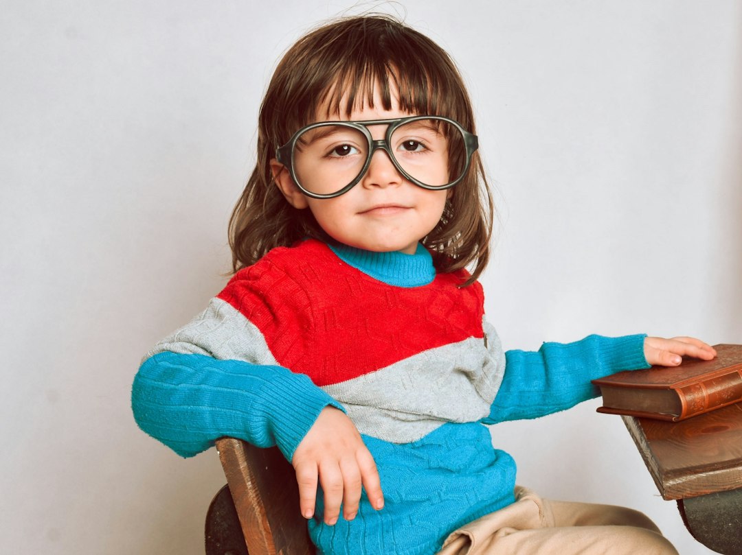 girl in red framed eyeglasses and gray sweater sitting on brown wooden chair JBcxO430PKM jpg