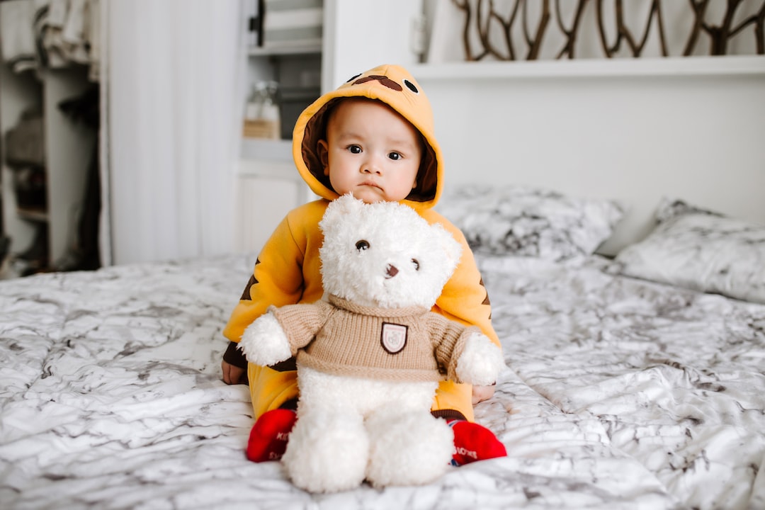 toddler sitting on bed beside white bear plush toy 6YMq73ydADI jpg